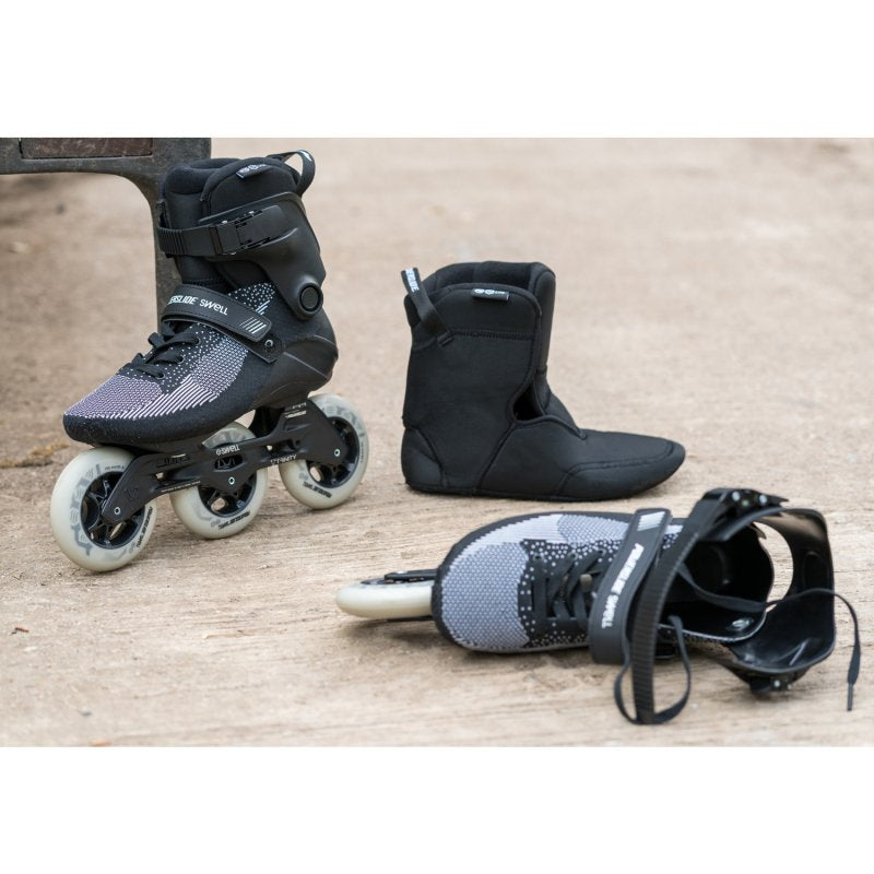 Powerslide Swell Lite Black 1OO Inline Skate outdoors, with one skate on it's side and the soft inner liner next to it.